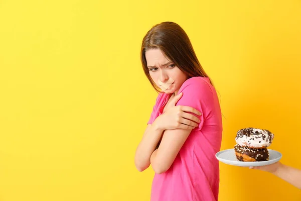 Ruka nabízí smutné ženě s nalepenými ústy chutné koblihy na barevném pozadí. Dietní koncept — Stock fotografie