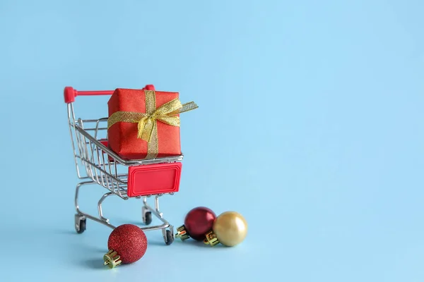 Carrinho de compras pequeno com caixa de presente sobre fundo de cor — Fotografia de Stock