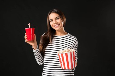 Siyah arka planda patlamış mısır ve soda içen genç bir kadın.