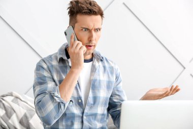 Şok olmuş genç adam evde telefonla konuşuyor.