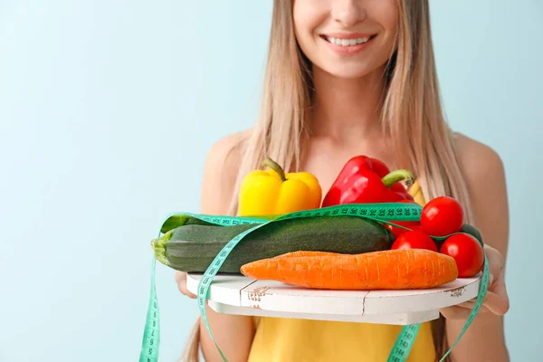 Happy woman with healthy vegetables and measuring tape on light background. Diet concept — Stock Photo, Image