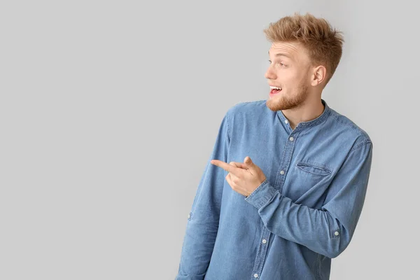 Surprised young man pointing at something on light background — Stockfoto