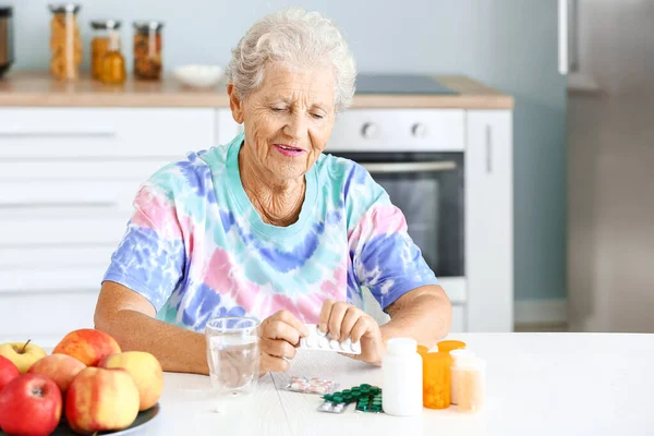 Elderly woman with pills at table in kitchen