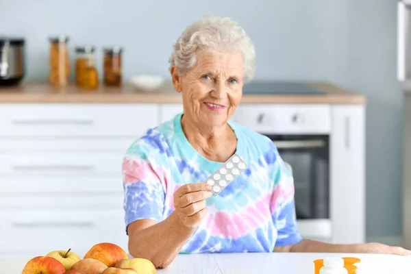 Elderly woman with pills at table in kitchen — Stock Photo, Image