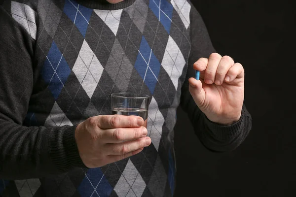 Elderly man taking pill on dark background, closeup