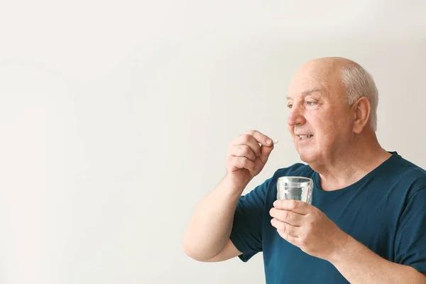 Hombre de edad avanzada que toma medicamentos sobre fondo claro —  Fotos de Stock