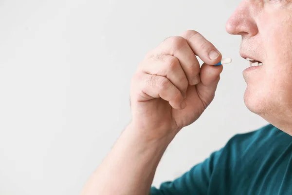 Elderly man taking medicine on light background, closeup — Stock Photo, Image