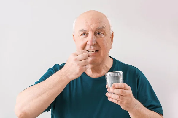 Elderly man taking medicine on light background — Stock Photo, Image