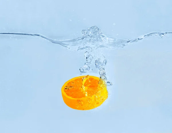 Queda de pedaço de laranja na água sobre fundo cinza — Fotografia de Stock