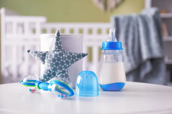 Bottle of milk, baby formula, rattle and toy star on table in room — Stock Photo, Image