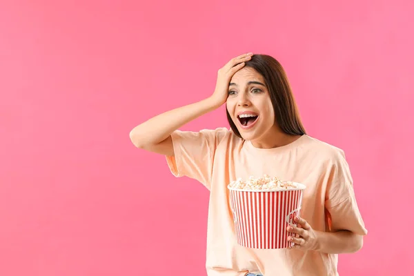 Überraschte Frau mit Popcorn auf farbigem Hintergrund — Stockfoto