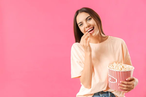 Young woman eating popcorn on color background — 图库照片