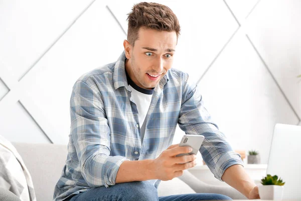 Překvapený mladý muž s mobilním telefonem v domácnosti — Stock fotografie