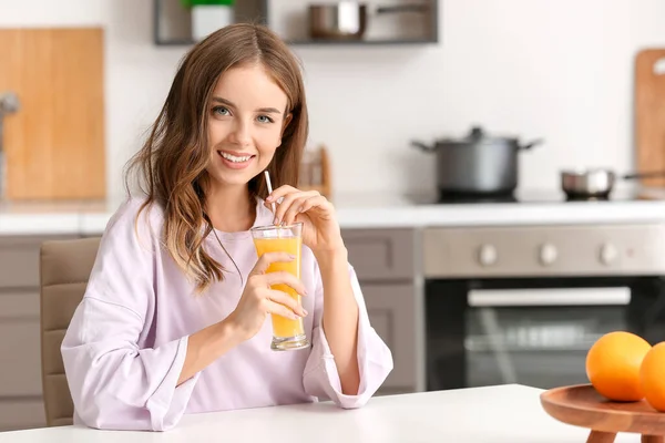 Mooie jonge vrouw drinken sinaasappelsap in keuken — Stockfoto