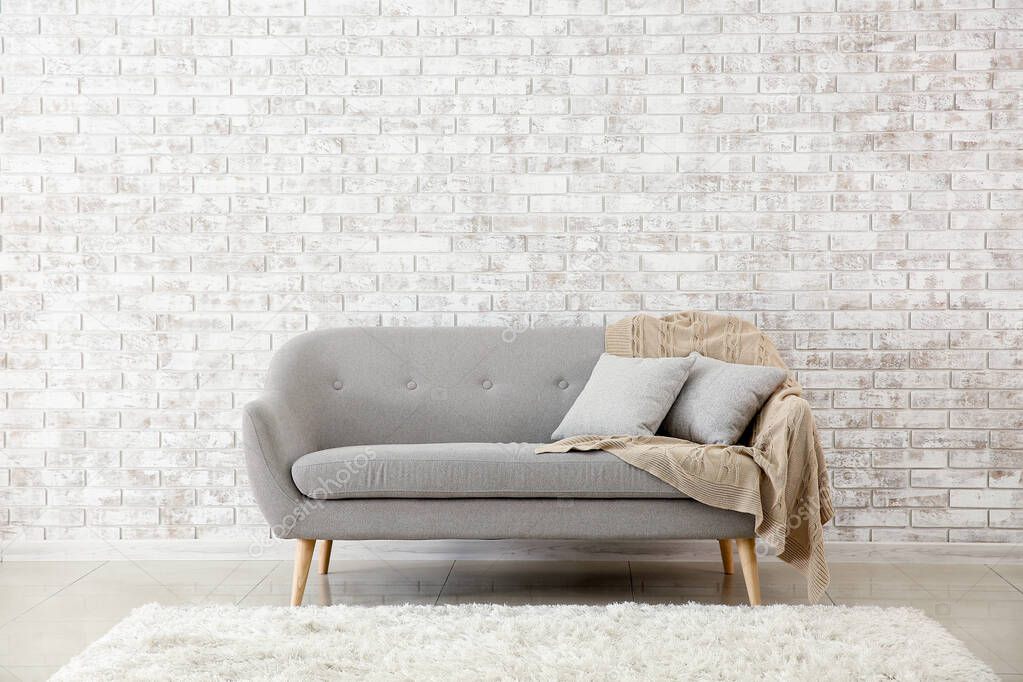 Comfortable sofa near brick wall in room