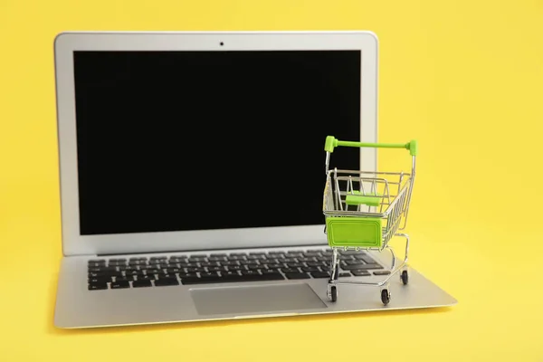 Laptop and small cart on color background. Internet shopping concept — Stock Photo, Image