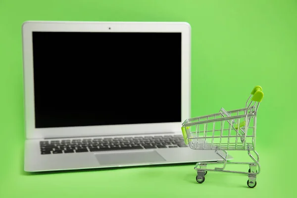 Laptop and small cart on color background. Internet shopping concept — Stock Photo, Image