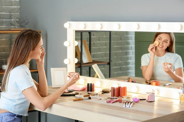 Beautiful young woman applying makeup in front of mirror — Stock Photo, Image