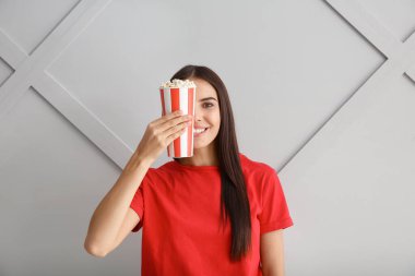 Gri arka planda patlamış mısırı olan genç bir kadın.