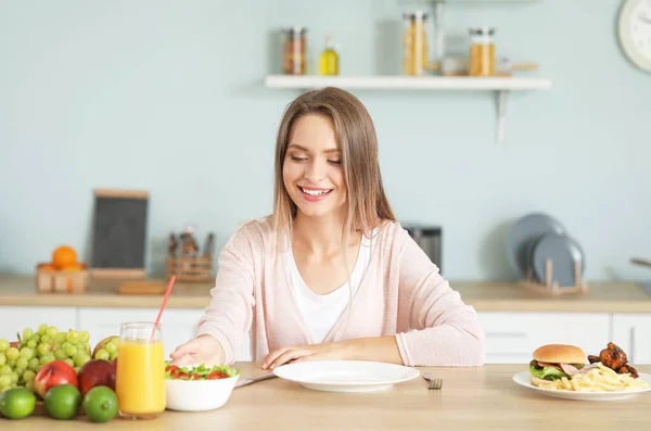 Mulher com alimentos saudáveis e não saudáveis na cozinha. Conceito de dieta — Fotografia de Stock