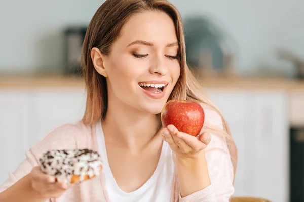 Woman with healthy apple and unhealthy donut in kitchen. Diet concept — Stock Photo, Image