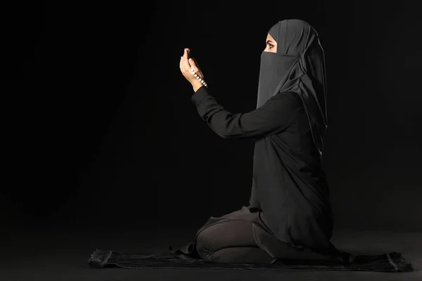 Beautiful Muslim woman praying against dark background — Stock Photo, Image