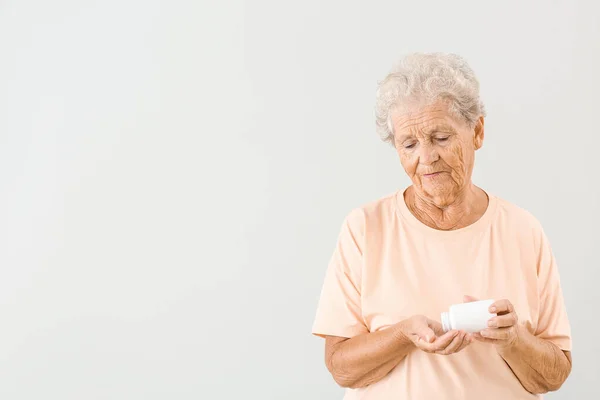 Elderly woman with pills on light background — Stock Photo, Image