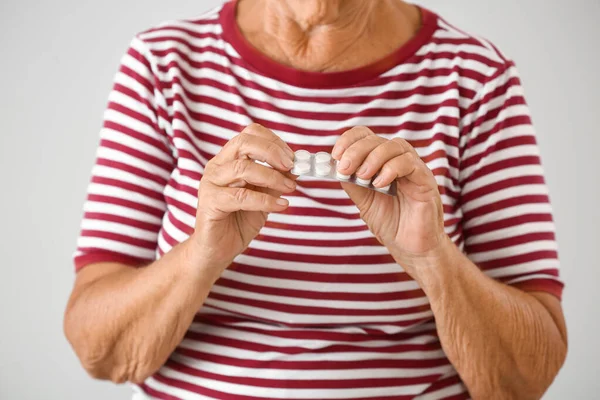 Oudere vrouw met pillen op lichte achtergrond, close-up — Stockfoto