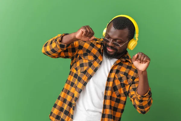 Handsome African-American man listening to music and dancing against color background — Stock Photo, Image