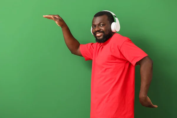 Handsome African-American man listening to music and dancing against color background — Stock Photo, Image