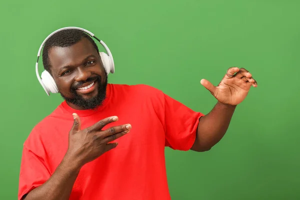 Handsome African-American man listening to music and dancing against color background — Stock Photo, Image