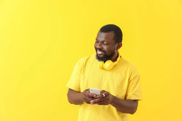 Handsome African-American man with headphones and mobile phone on color background — Stock Photo, Image