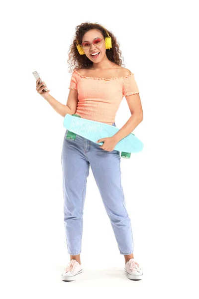 Beautiful African-American woman with skateboard listening to music on white background — Stock Photo, Image