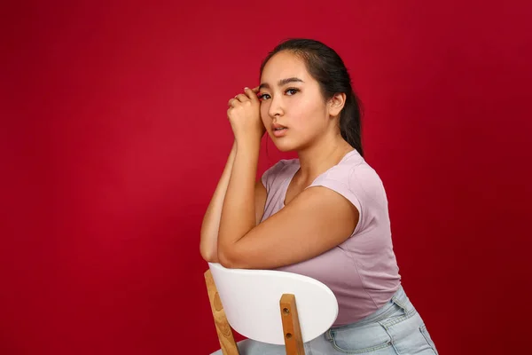 Portrait of beautiful Asian woman sitting on chair against color background — Stock Photo, Image
