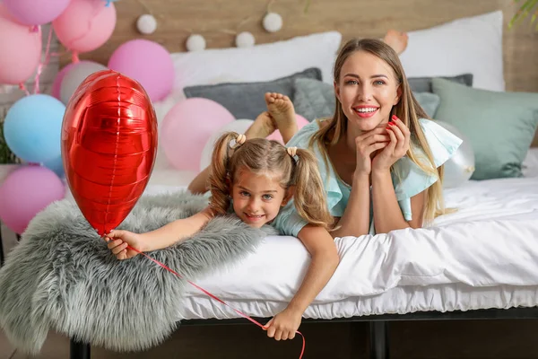 Beautiful young woman and her little daughter with air balloon lying on bed — Stock Photo, Image