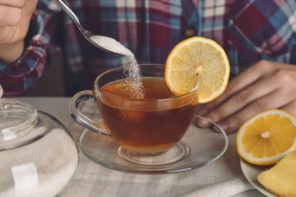 Femme versant du sucre dans une tasse avec du thé chaud à table, gros plan — Photo