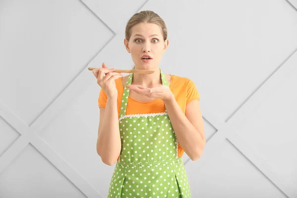 Sorpresa giovane donna in grembiule e con cucchiaio su sfondo chiaro — Foto Stock
