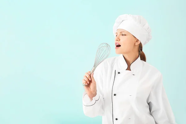 Piękna kucharka używająca trzepaczki jako mikrofonu do śpiewania na jasnym tle — Zdjęcie stockowe