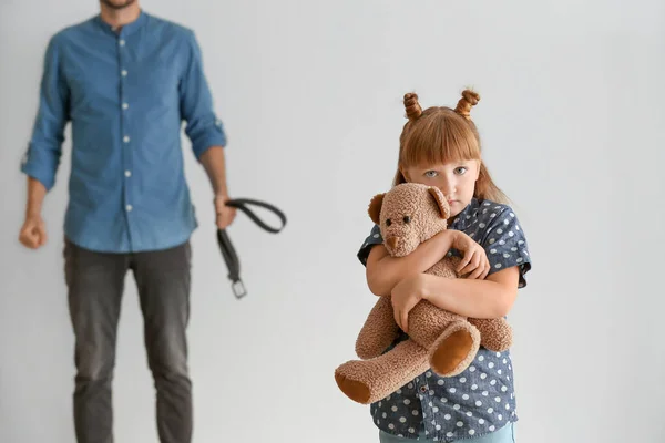 Hombre amenazando a su pequeña hija contra un fondo claro. Concepto de castigo físico — Foto de Stock