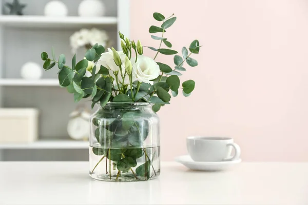 Florero con hermosas flores y taza de té en la mesa en la habitación — Foto de Stock