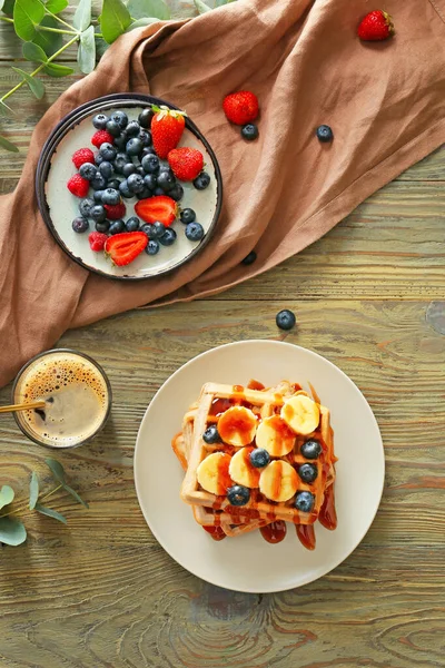 Plates with sweet tasty waffles, berries and coffee on table — Stock Photo, Image
