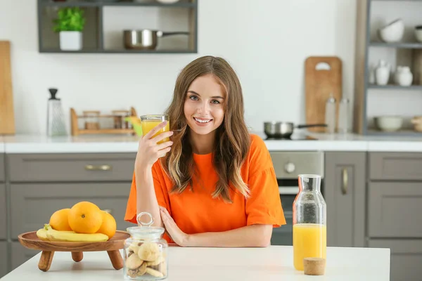 Güzel genç bayan mutfakta portakal suyu içiyor. — Stok fotoğraf
