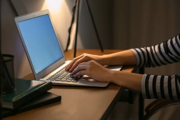 Ung kvinna som arbetar på laptop vid bordet på kvällen — Stockfoto