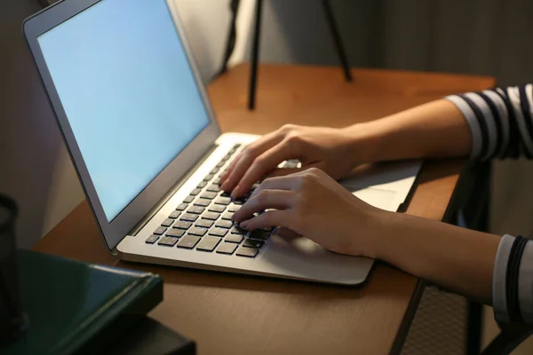 Ung kvinna som arbetar på laptop vid bordet på kvällen — Stockfoto