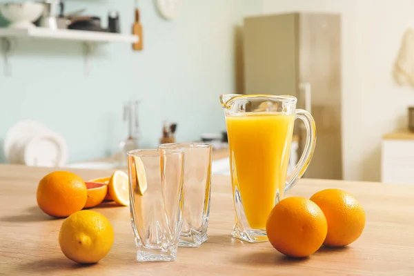 Jug of fresh fruit juice and empty glasses on table — Stock Photo, Image