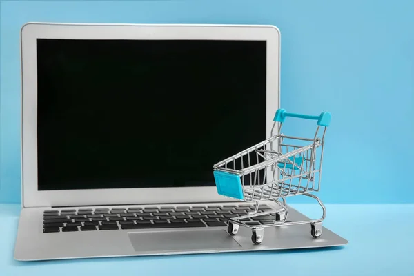 Laptop e carrinho pequeno em fundo de cor. Conceito de compras na Internet — Fotografia de Stock