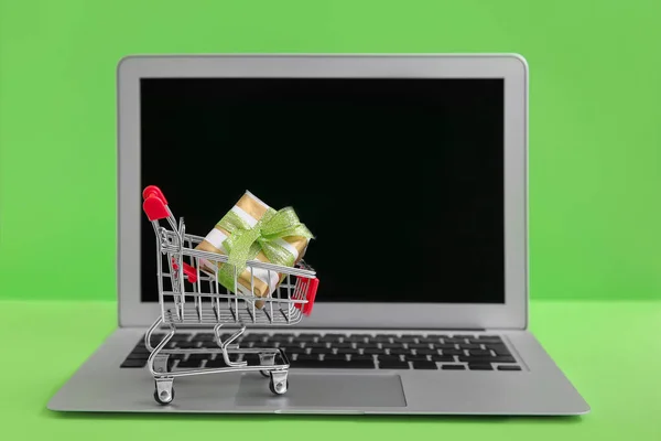 Laptop and small cart with gift on color background. Internet shopping concept — Stock Photo, Image