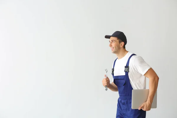 Running car mechanic with laptop on light background — Stock Photo, Image