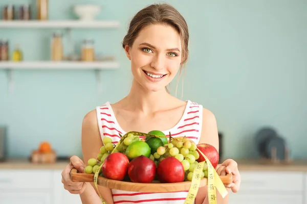 Mujer joven con frutas saludables y cinta métrica en la cocina. Concepto de dieta —  Fotos de Stock