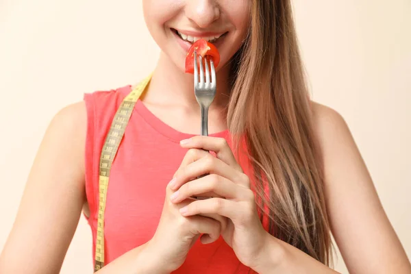 Kobieta ze świeżym pomidorem na widelcu i taśmą pomiarową na jasnym tle. Koncepcja diety — Zdjęcie stockowe
